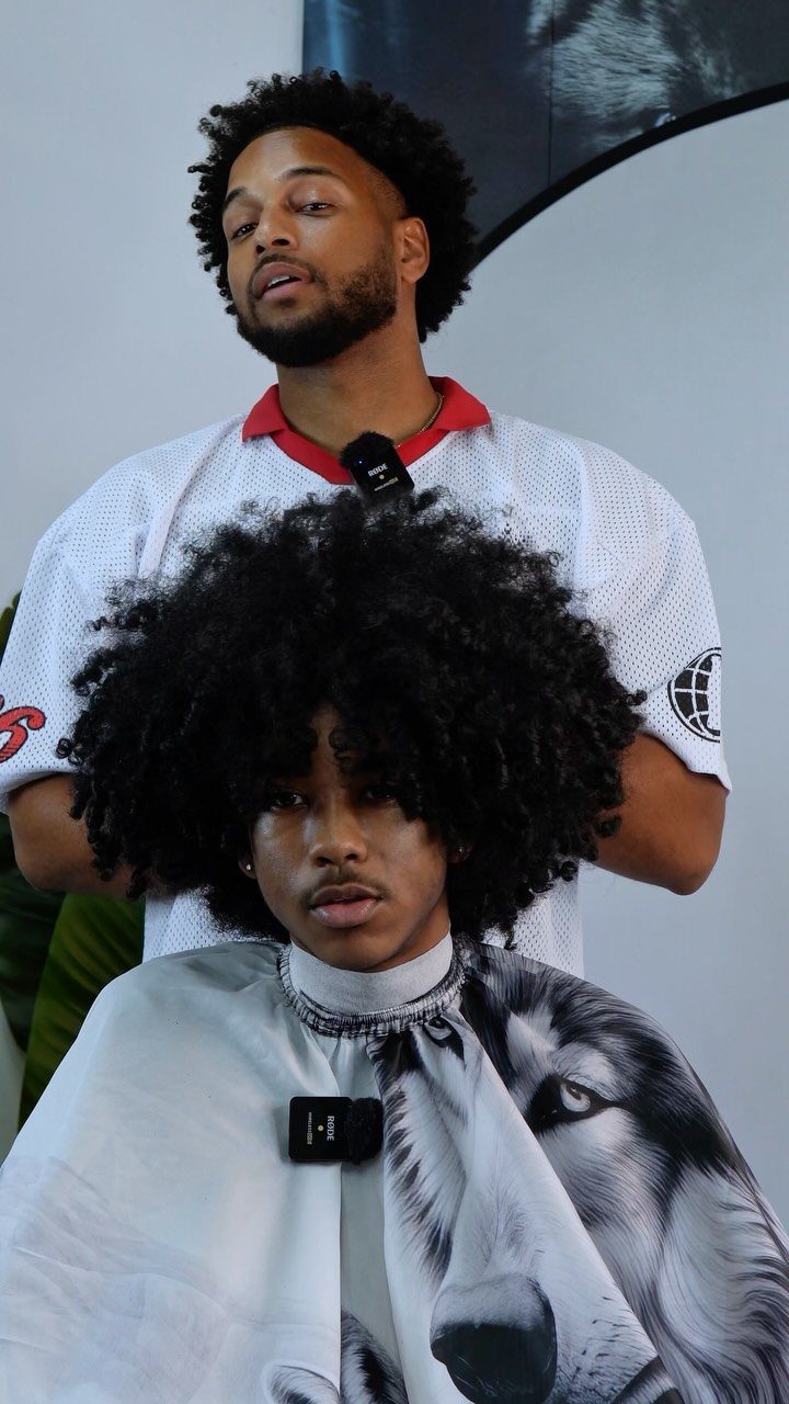 Young man with a large, voluminous blowout afro hairstyle wearing a barber cape.