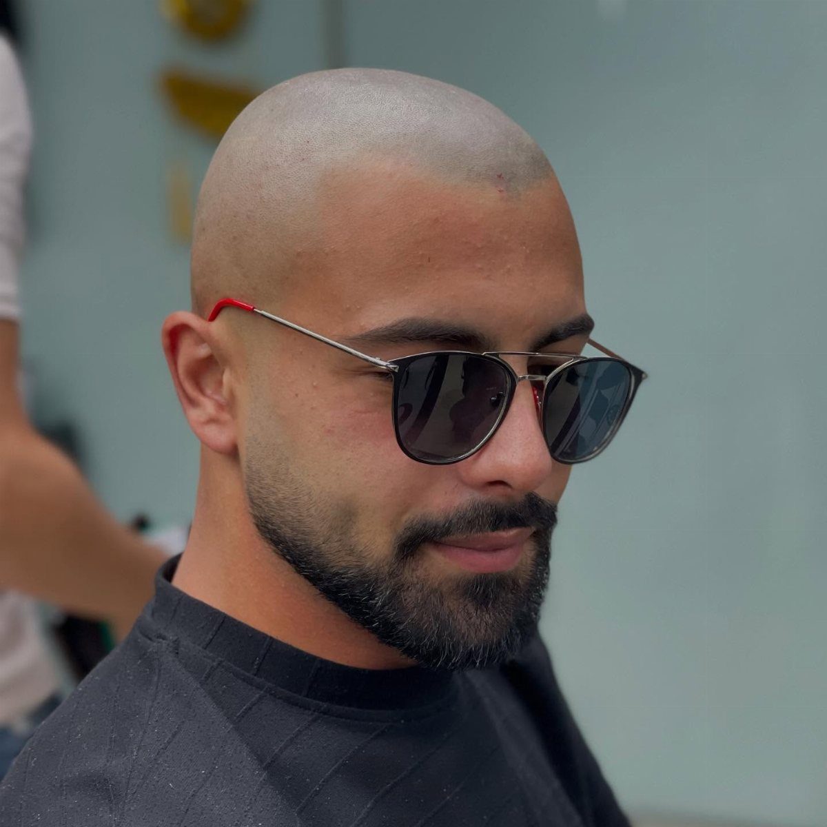 Man with a bald head and full black beard wearing aviator sunglasses.