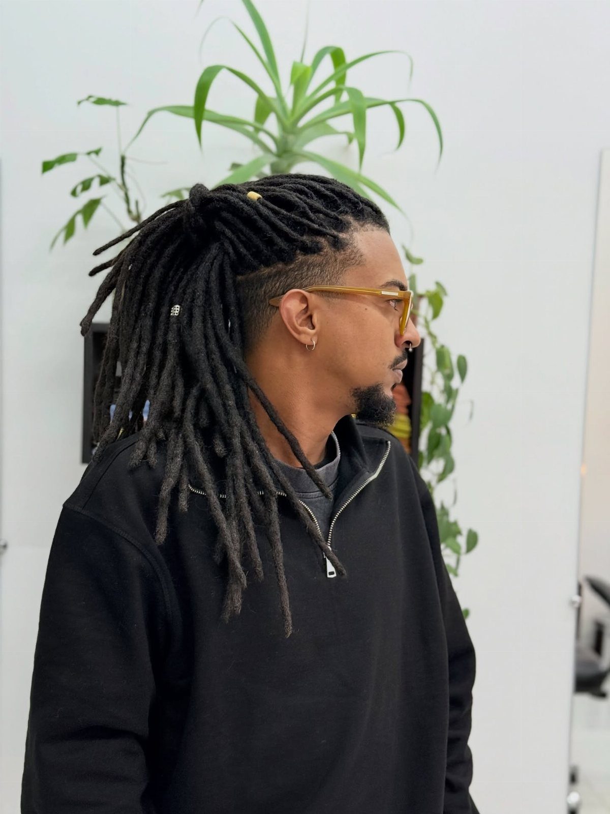 Man with long black dreadlocks tied back and a shaved undercut side profile