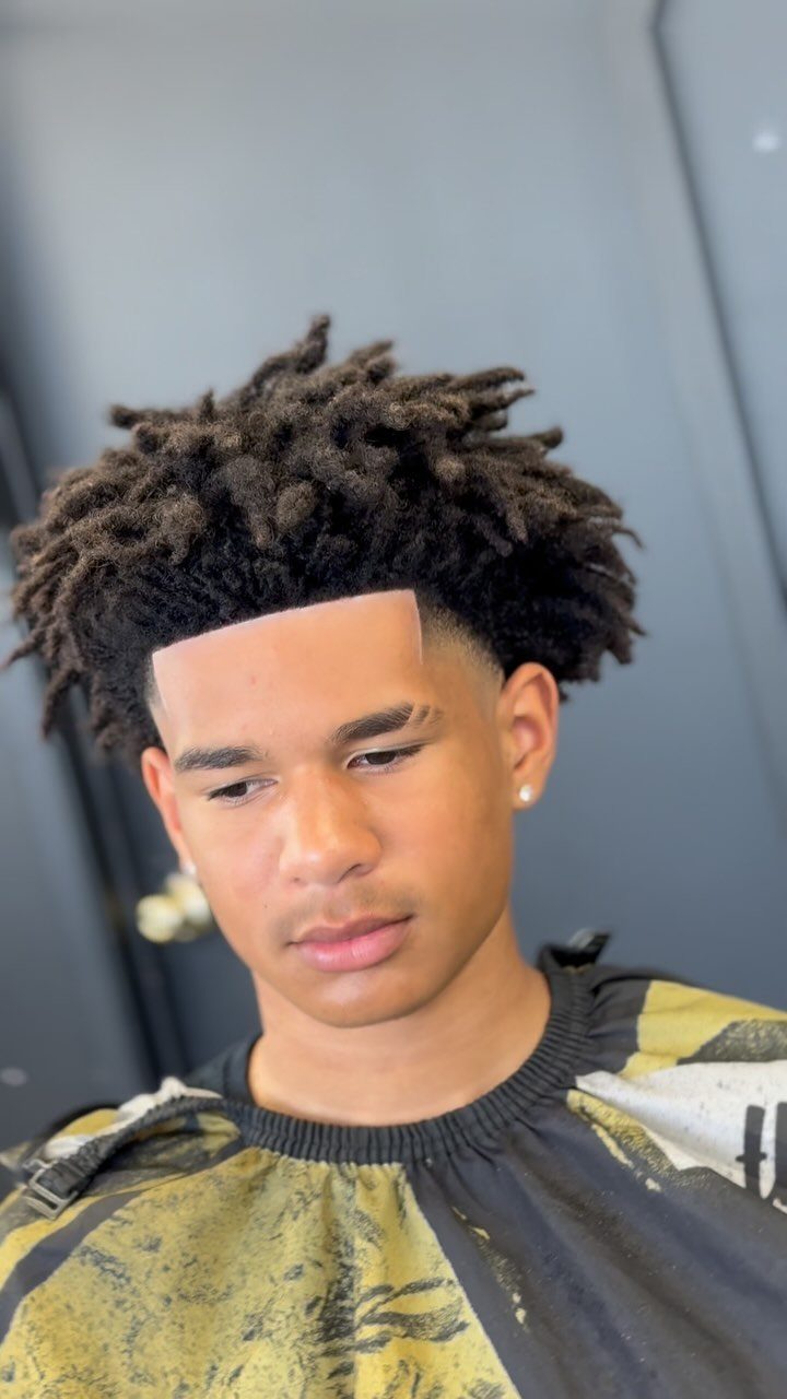Young man with freeform locs and a clean line-up wearing a barber cape.