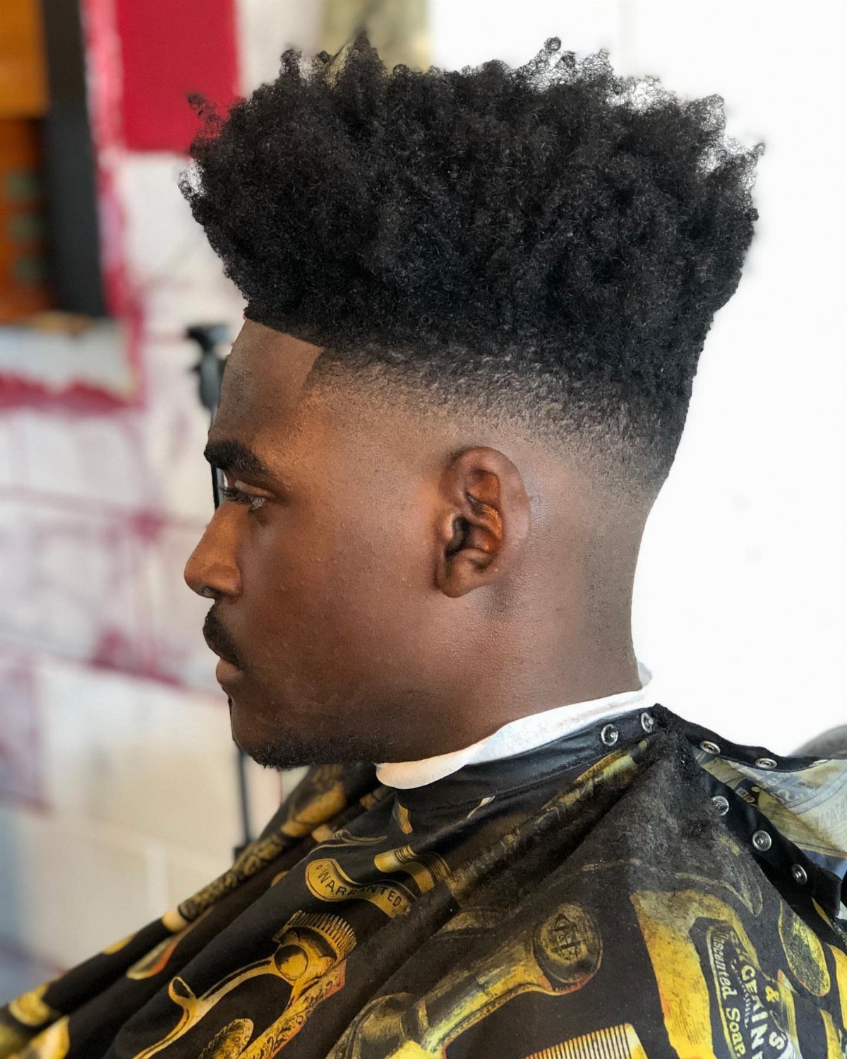 Black man with a high-top fade haircut and textured crown wearing a barber cape.