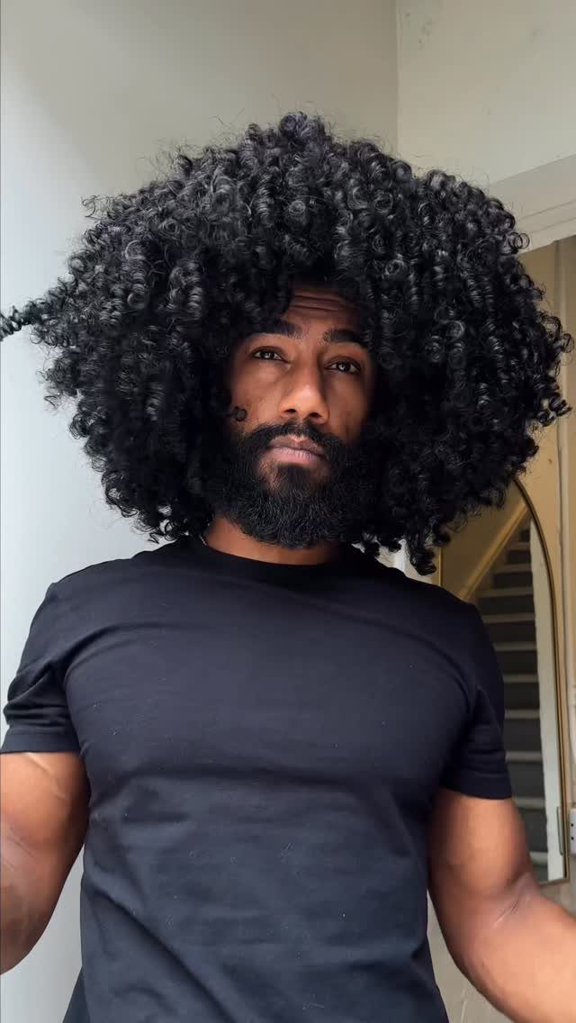 Man with a large, voluminous black afro and groomed beard wearing a black t-shirt.