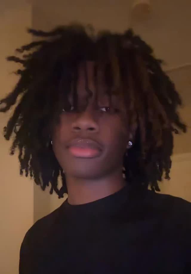 Young Black man with long, voluminous dreadlocks and a black t-shirt.