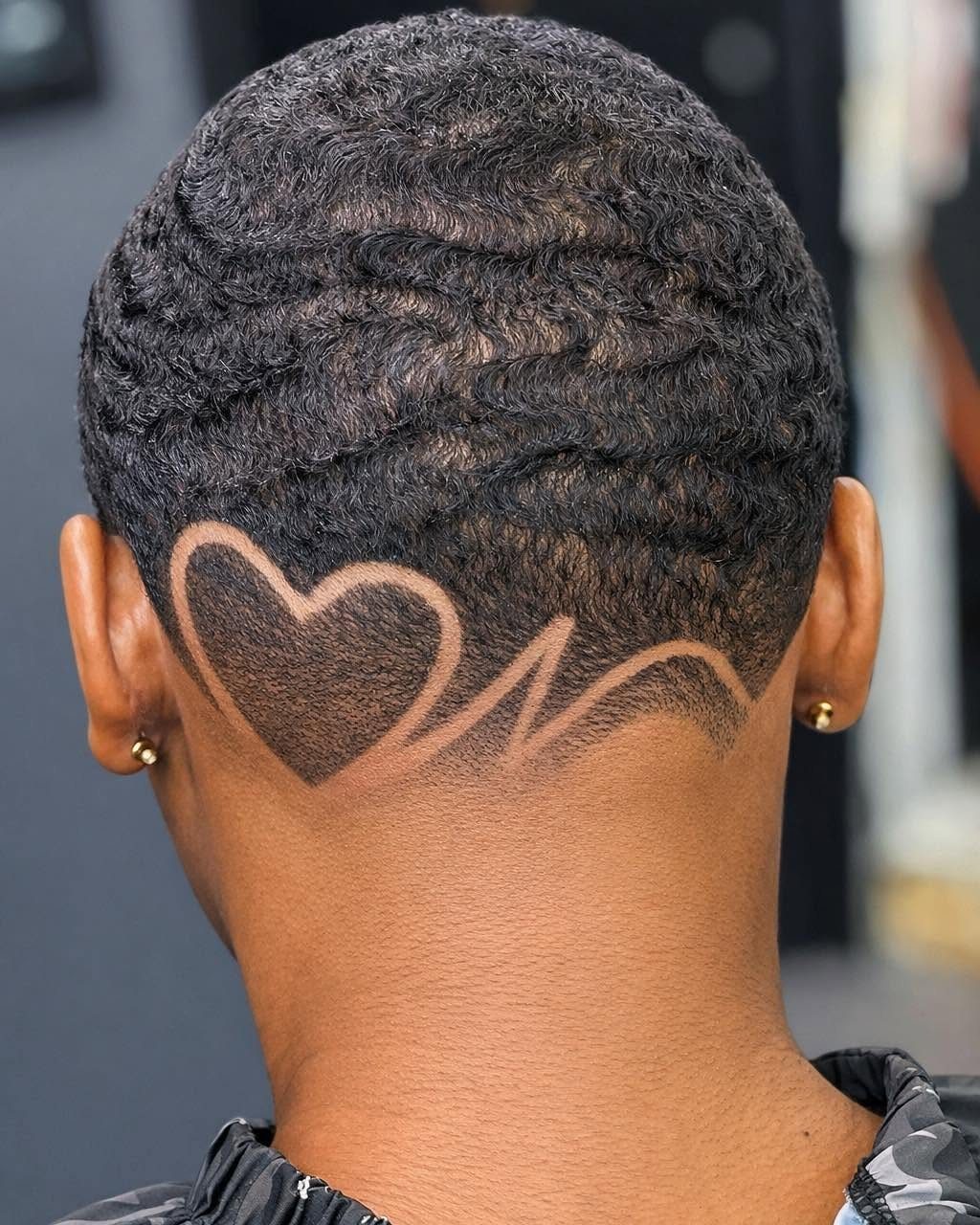 Short black wavy hair with a heart shape shaved into the nape.
