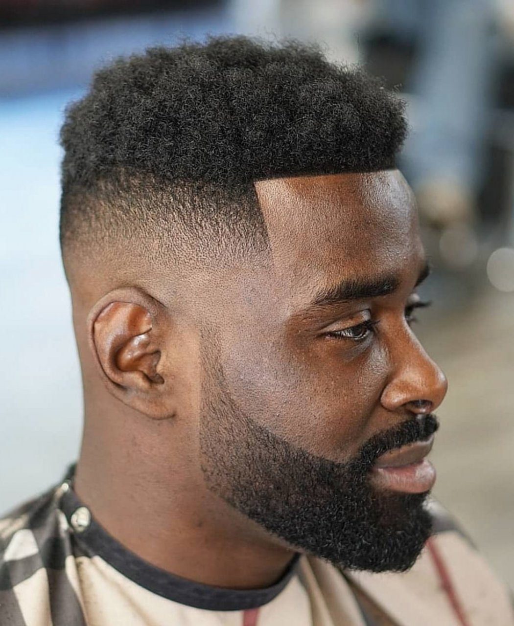 Black man with a short textured afro, skin fade, and groomed full beard.