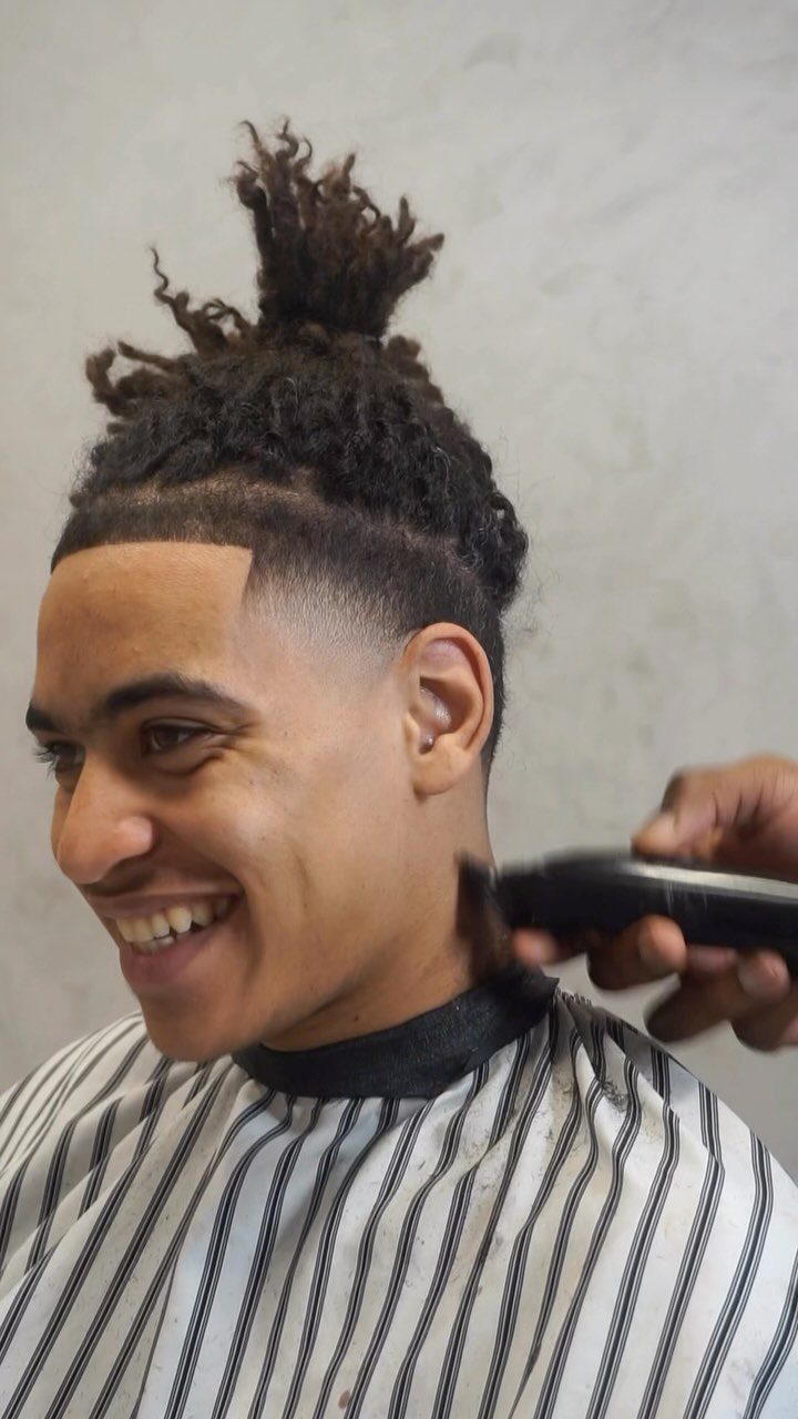 Man with short locs and a skin fade getting a haircut from a barber.