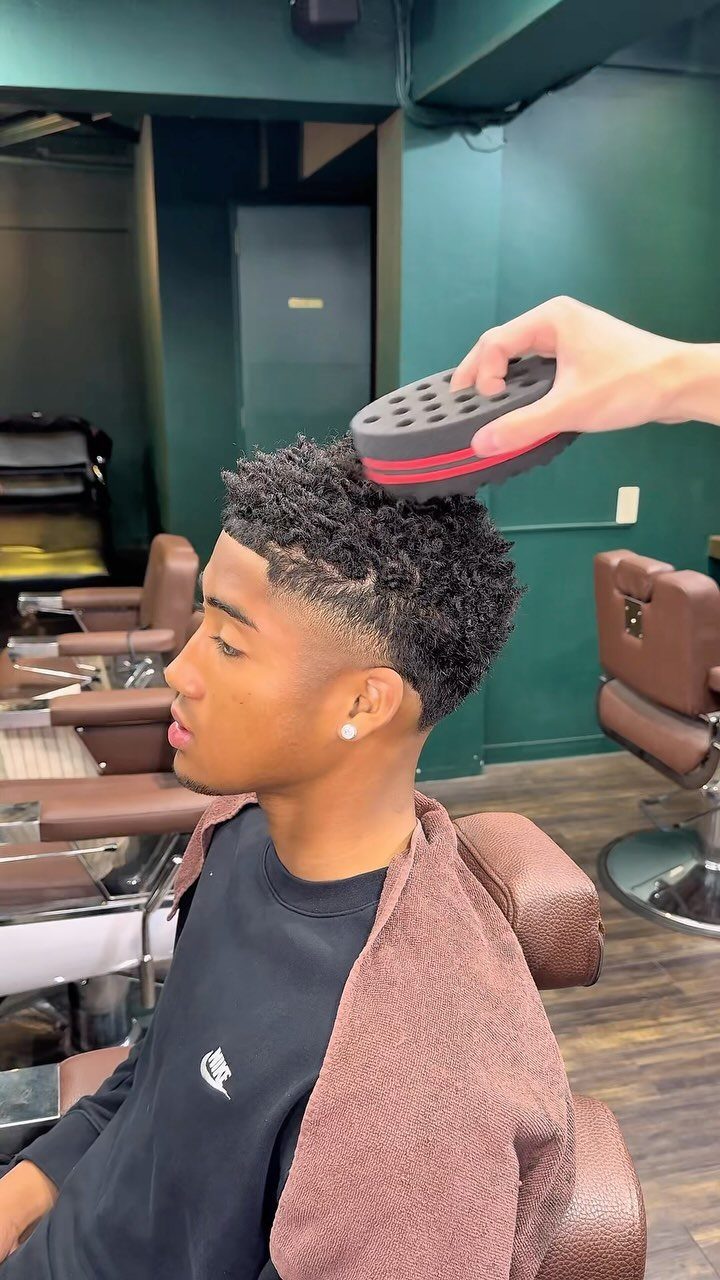 Young Black man with a short afro and fade getting styled with a sponge.
