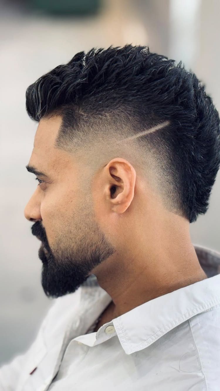 Man with a textured fade haircut, shaved line detail, and a groomed beard.