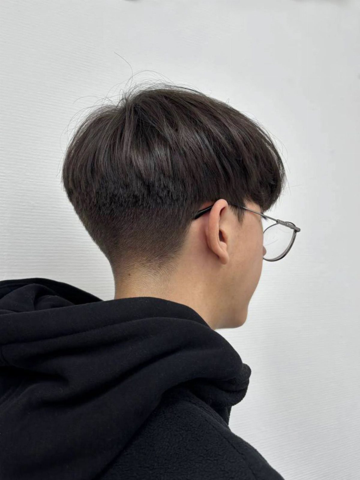 Man with a bowl cut and glasses wearing a black hoodie.