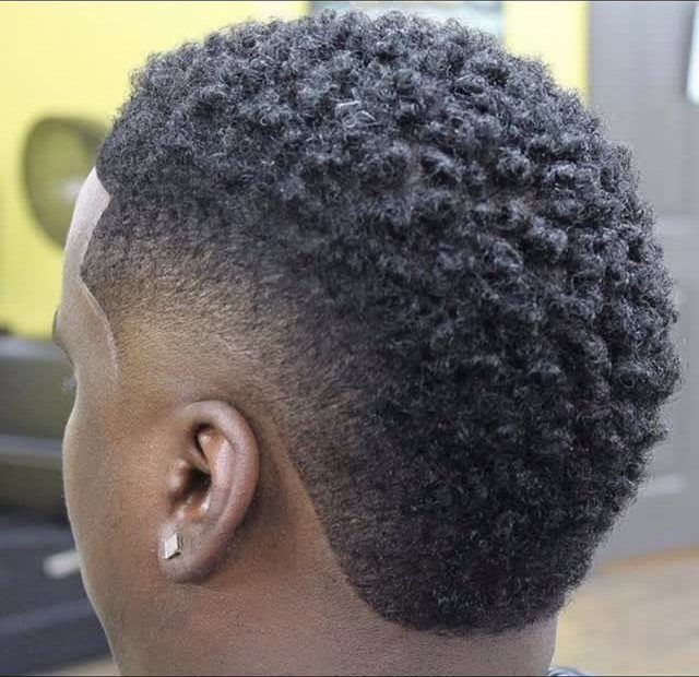 Man with a burst fade haircut showing curly hair and tapered sides around ear.