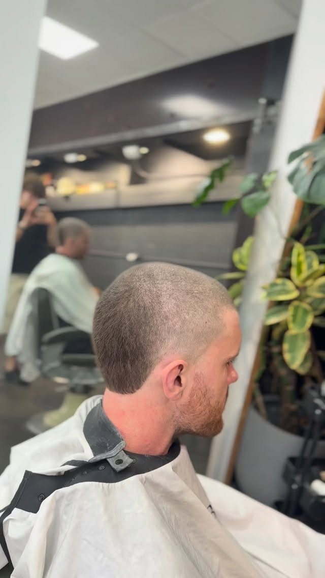 Man with a short buzz cut wearing a white barber cape in a shop.