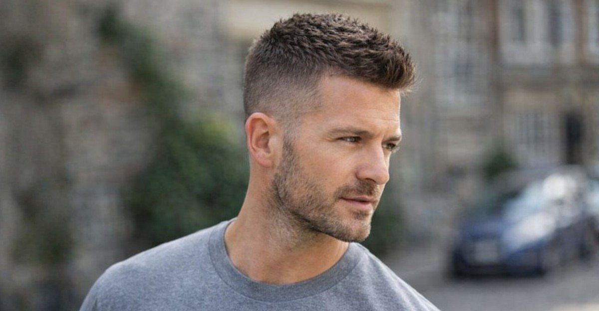 Man with a crew cut hairstyle and short beard wearing a grey t-shirt.