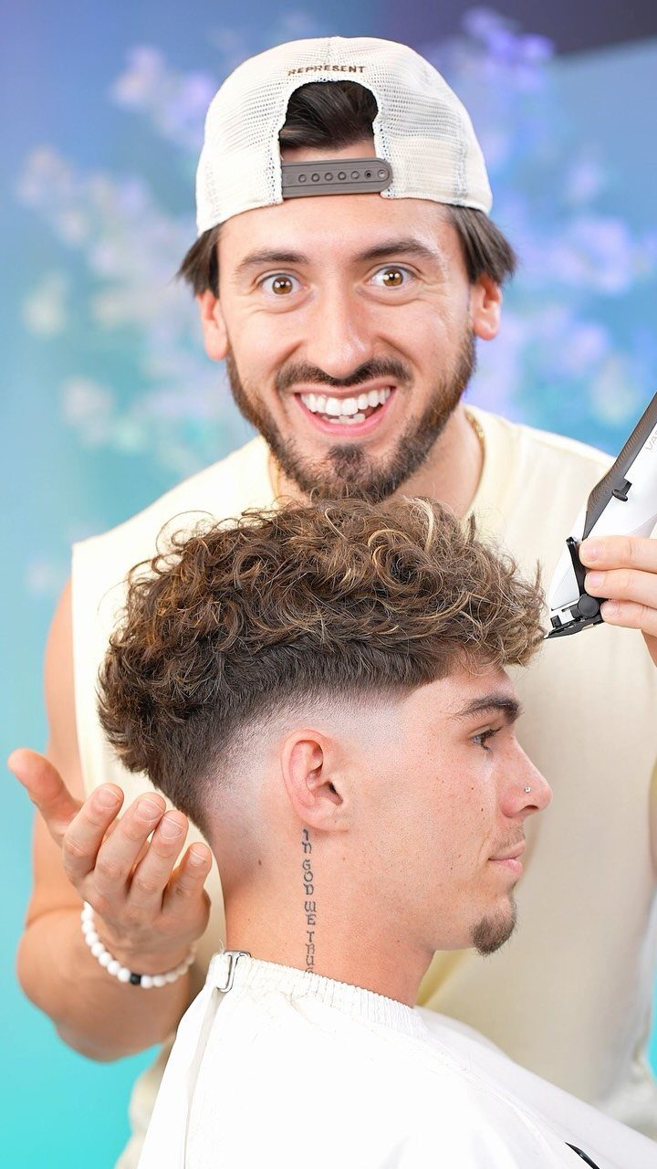 Barber trimming a man's curly hair with a drop fade haircut.