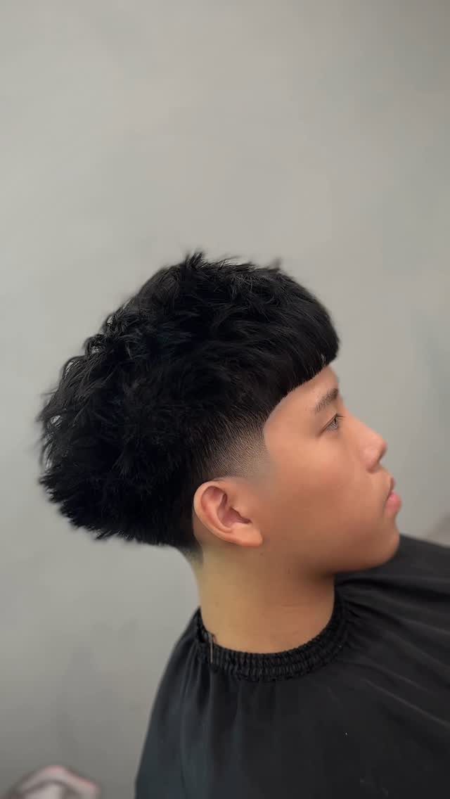 Young man with a black Edgar haircut featuring a blunt fringe and skin fade.