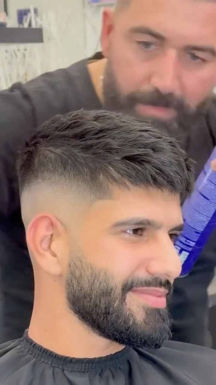 Man with a French crop haircut and beard in a barbershop setting.