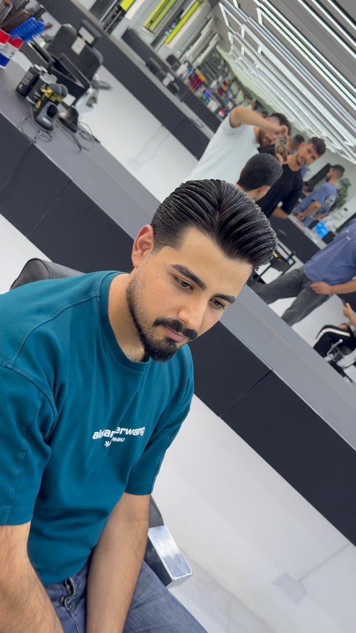 Man with a styled pompadour haircut and beard sitting in a barbershop.