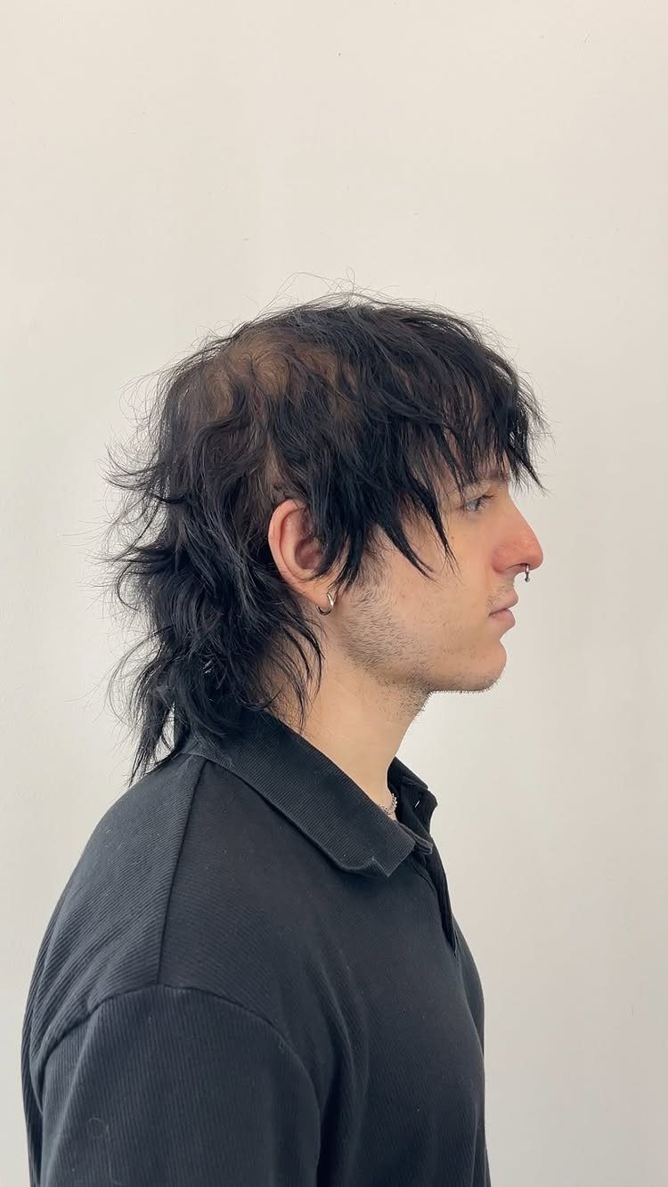 Man with a messy black shag haircut and fringe in side profile.