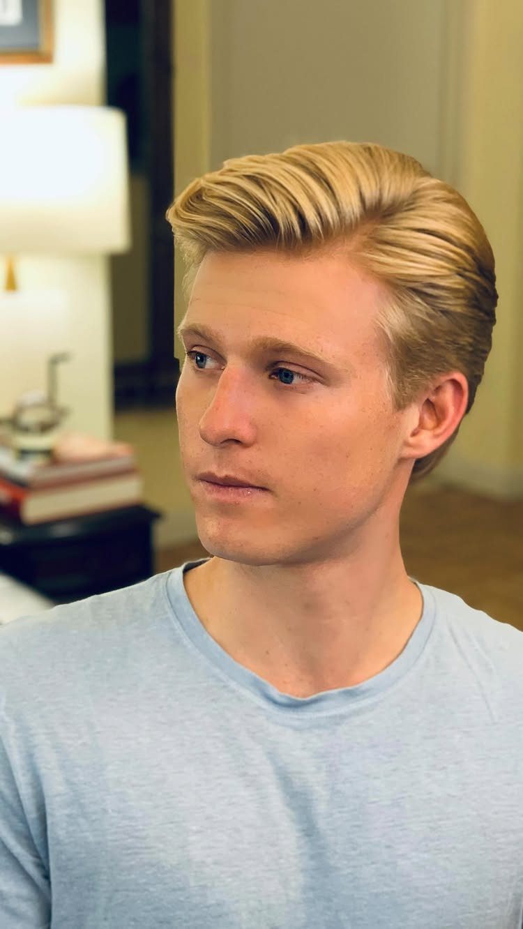 Blonde man with a classic side part haircut and light blue t-shirt.