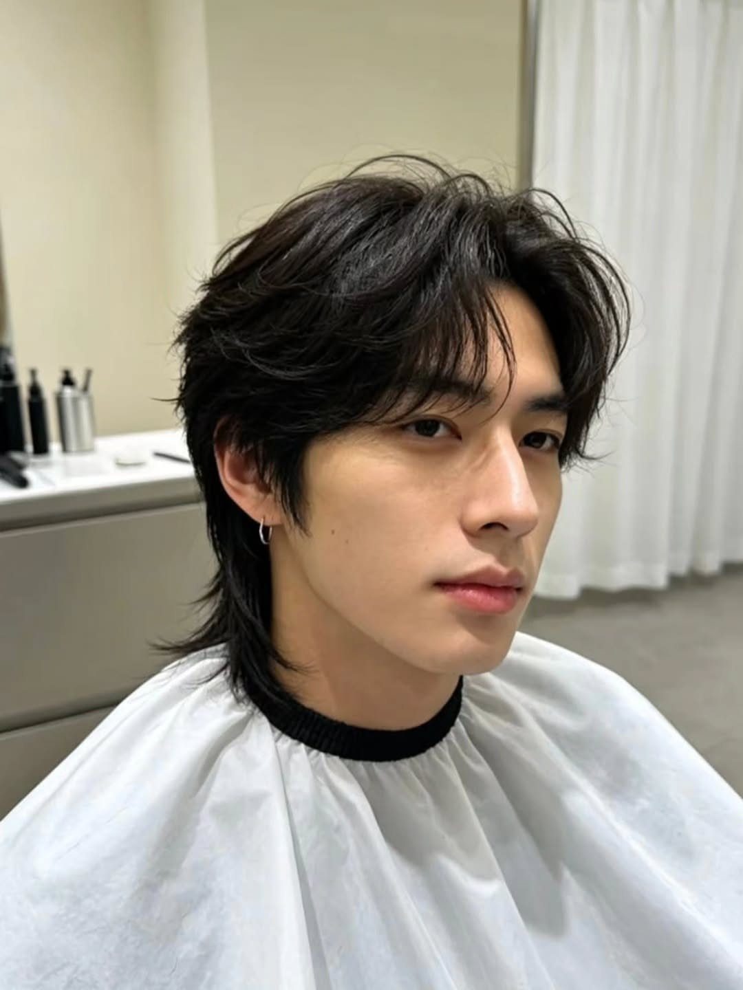 Young man with dark straight hair styled in curtain bangs and a middle part.