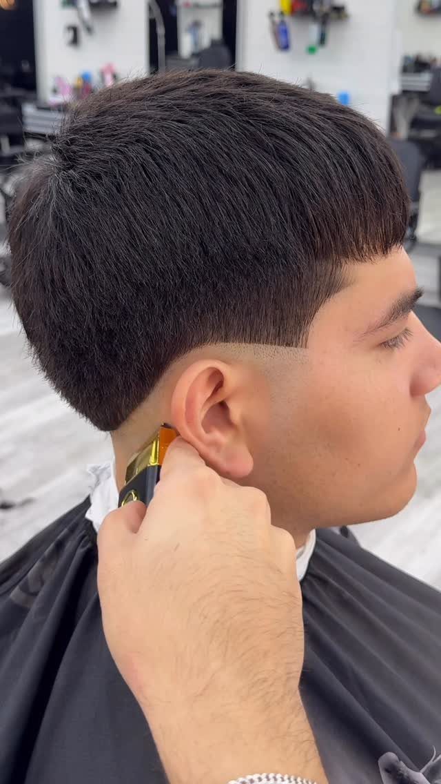 Man with a drop fade haircut and blunt fringe getting trimmed with clippers.