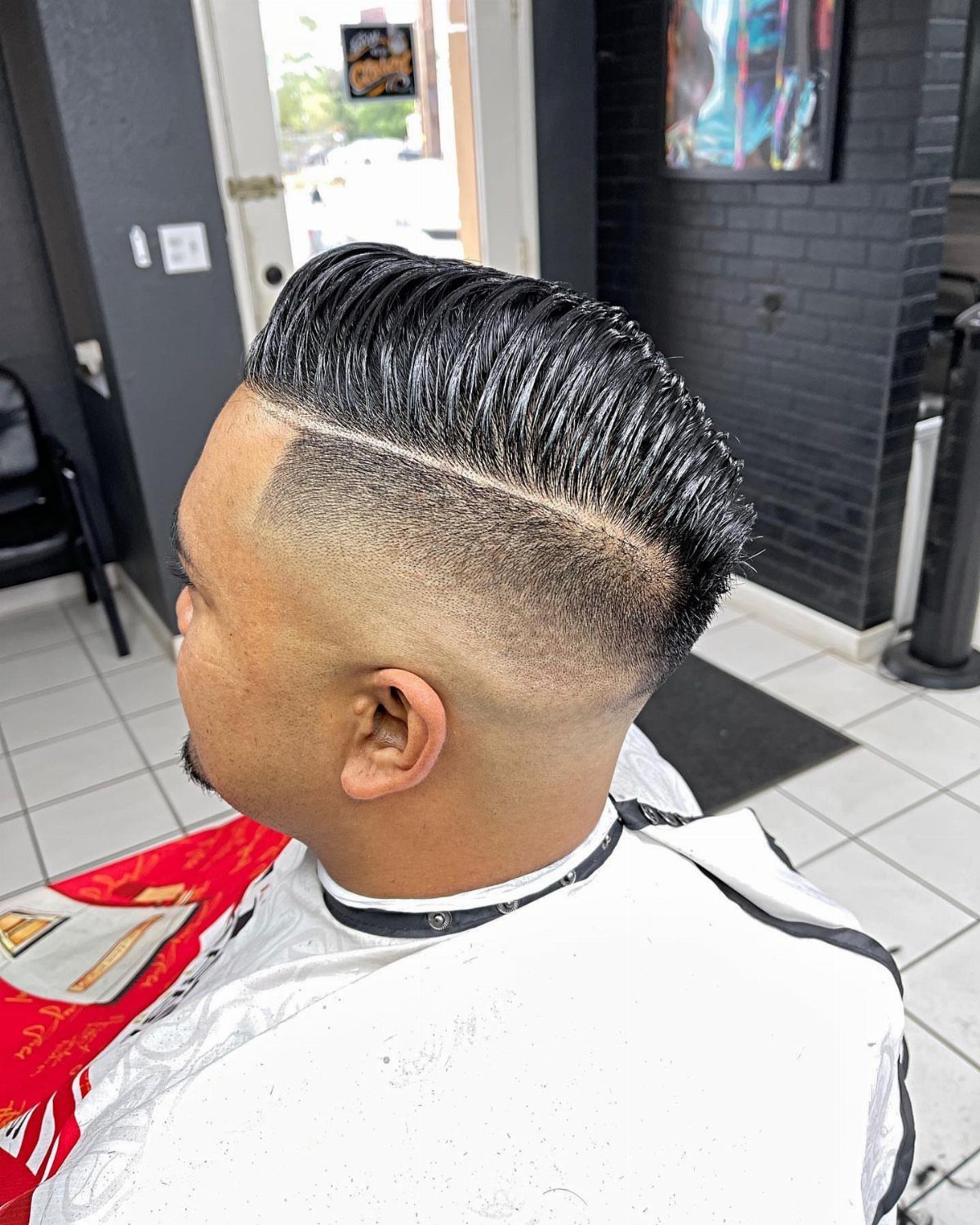Man with a hard part fade and slicked back dark straight hair.