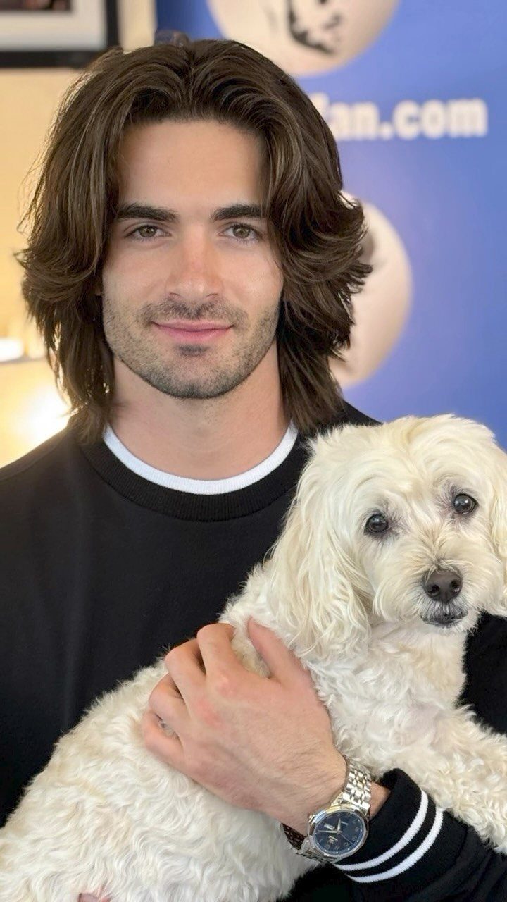 Man with long brown straight hair holding a small white fluffy dog.