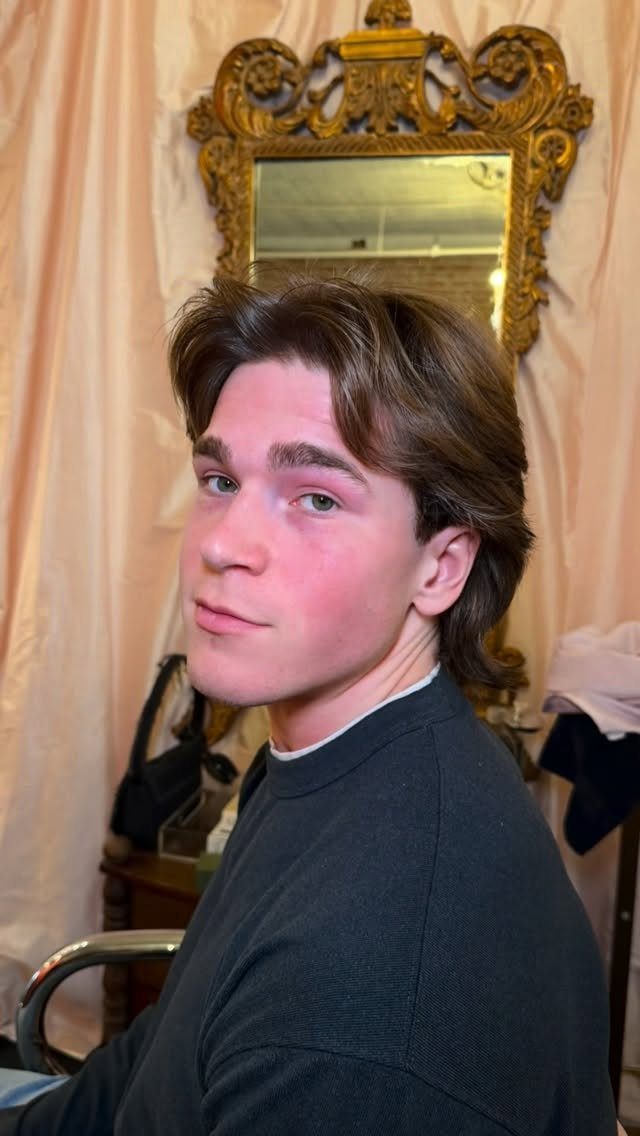 Young man with brown straight hair styled in a center-parted modern curtains haircut.