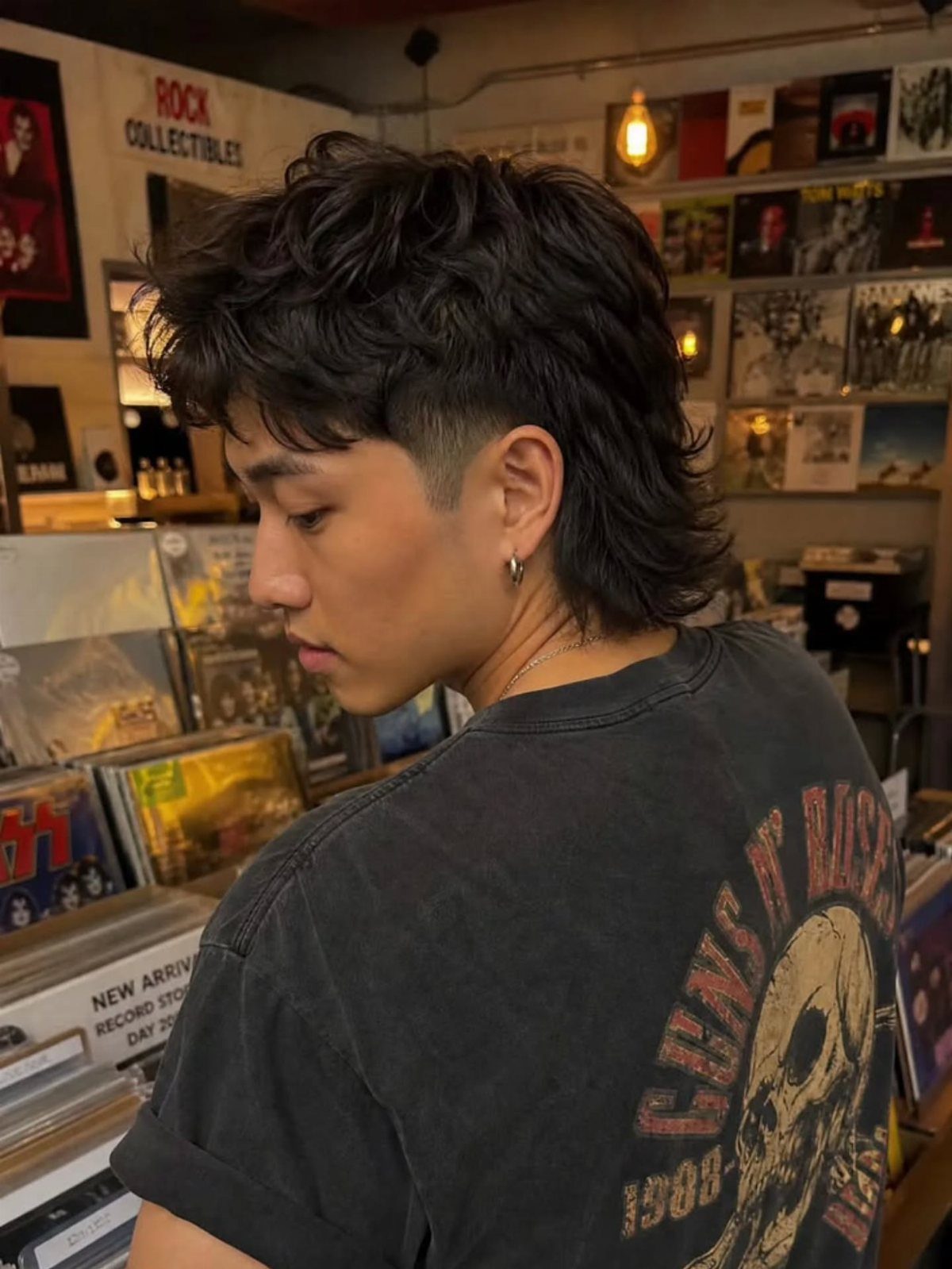 Young man with a modern mullet haircut standing in a record store.