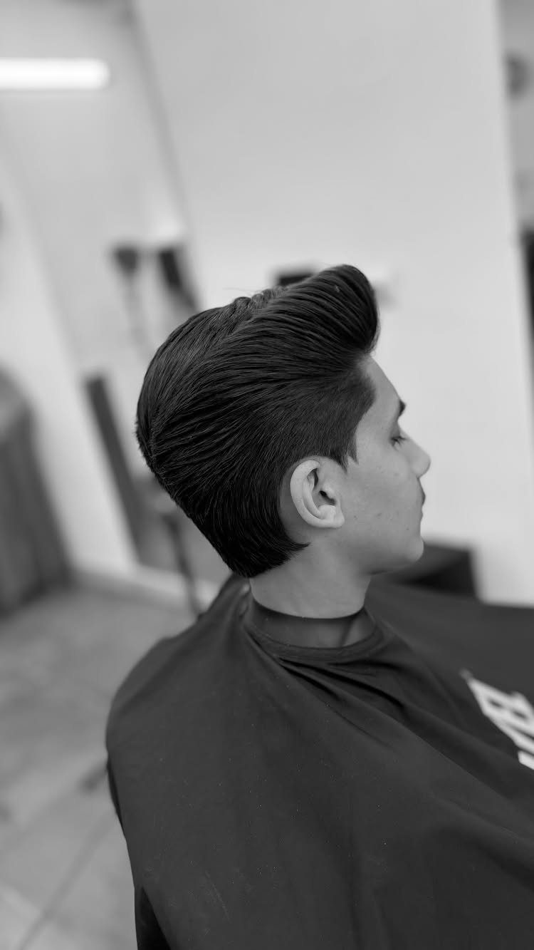 Young man with a high volume pompadour hairstyle in a barber shop setting.