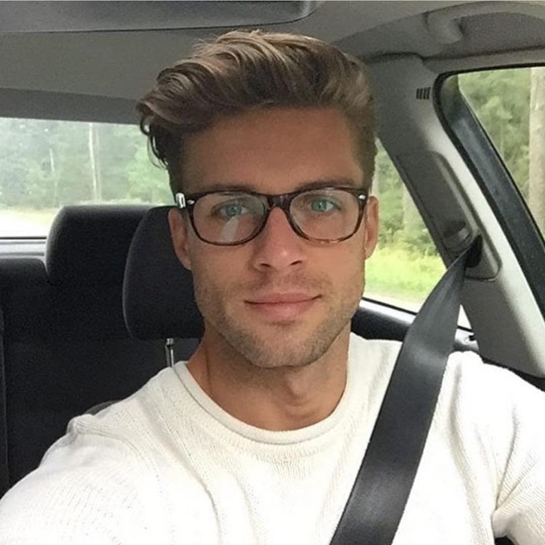Man with a quiff hairstyle and glasses sitting inside a car.