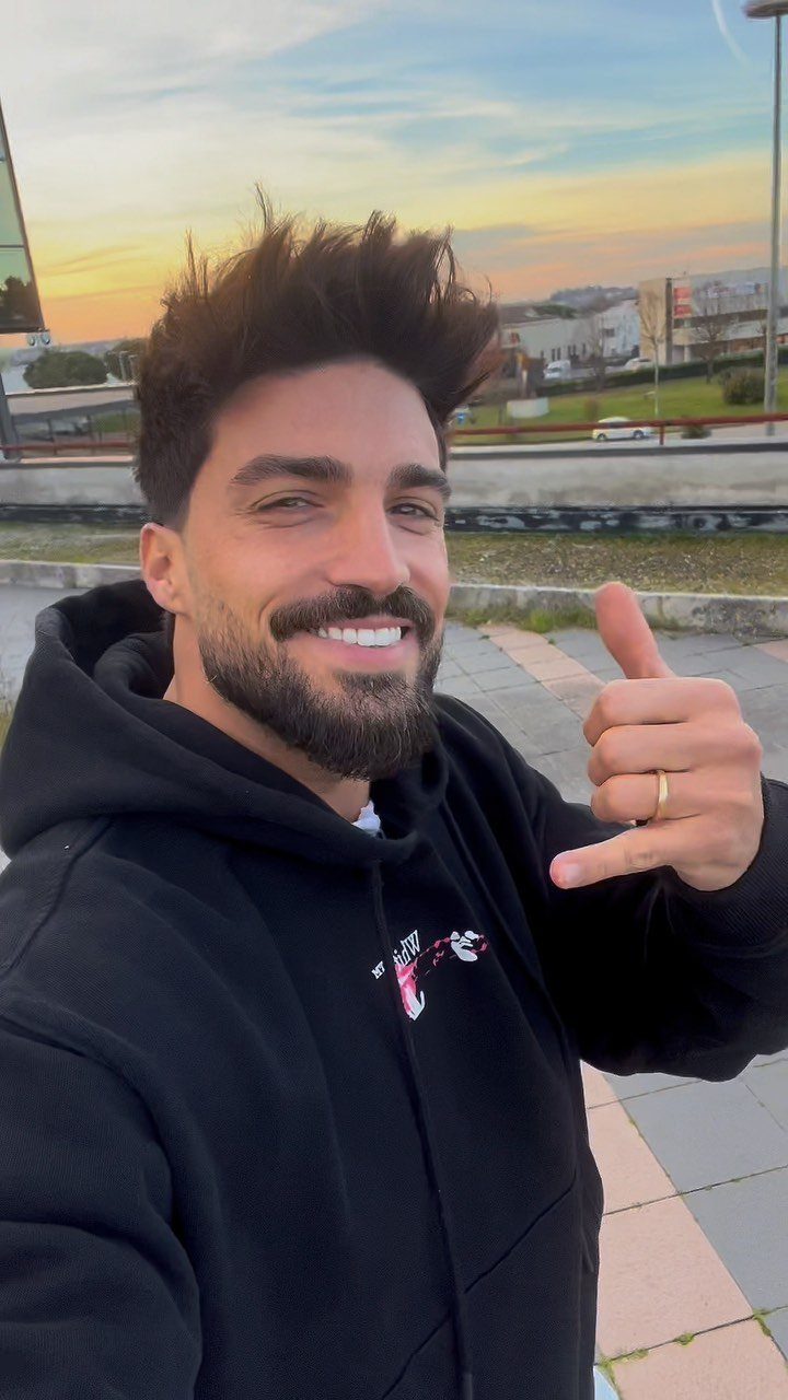 Smiling man with spiky brown hair and beard wearing a black hoodie outdoors.