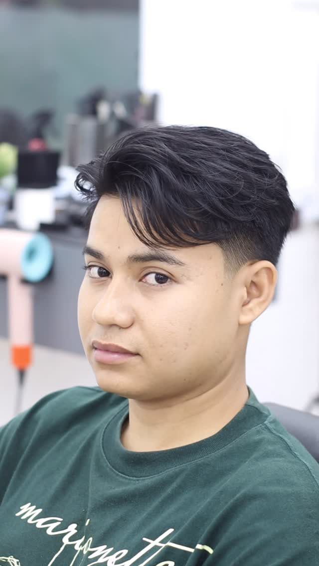 Man with straight black hair styled in a side swept fringe and tapered sides.