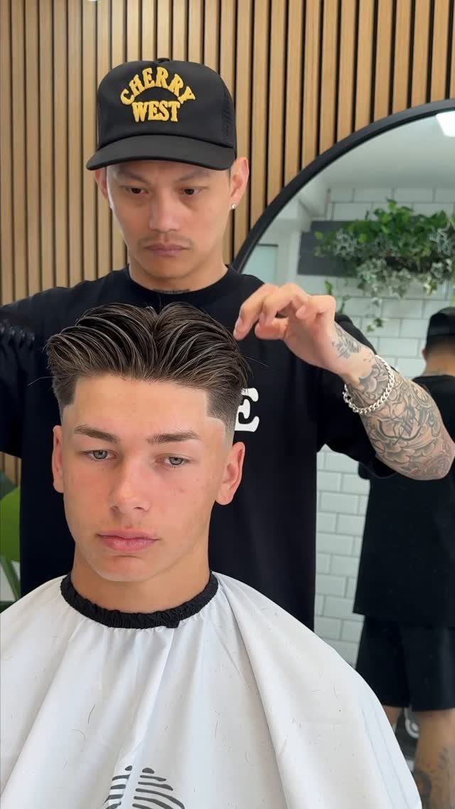 Barber styling a young man's hair with a high skin fade and swept-back top.
