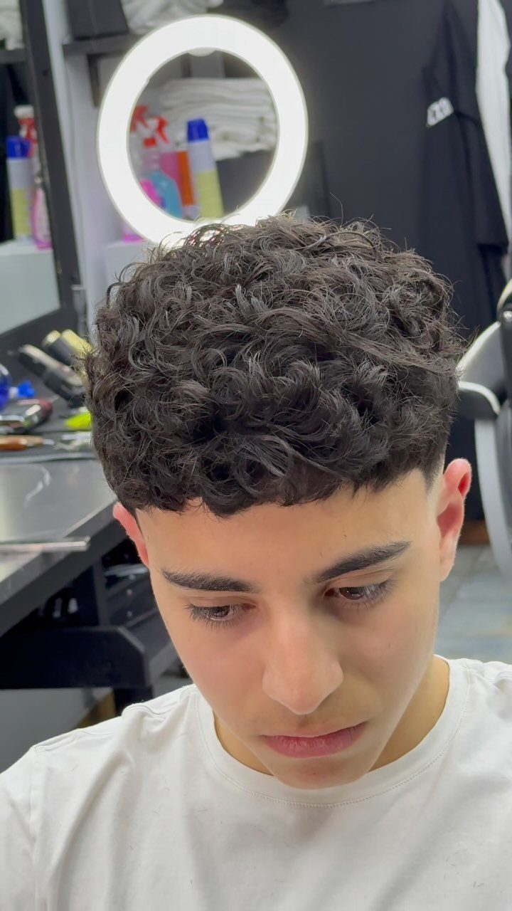 Young man with a curly fringe haircut and short sides in a barbershop.