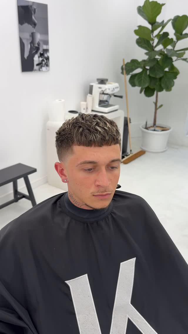 Man with a textured French crop haircut and faded sides in a barbershop.