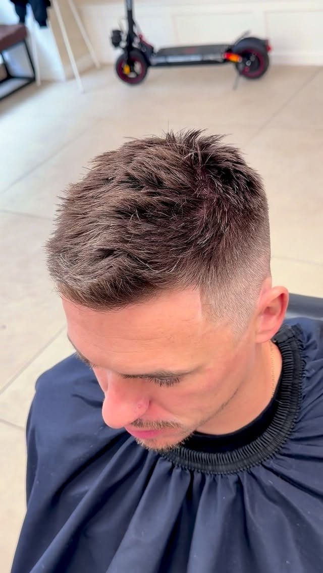 Man with a high fade haircut and textured top wearing a barber cape.