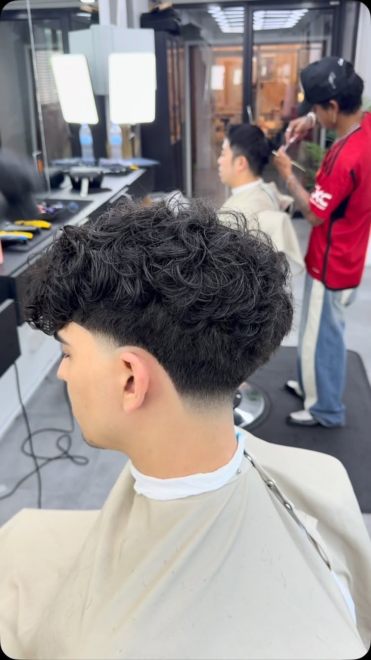 Man with curly hair and a low taper fade at a barbershop.