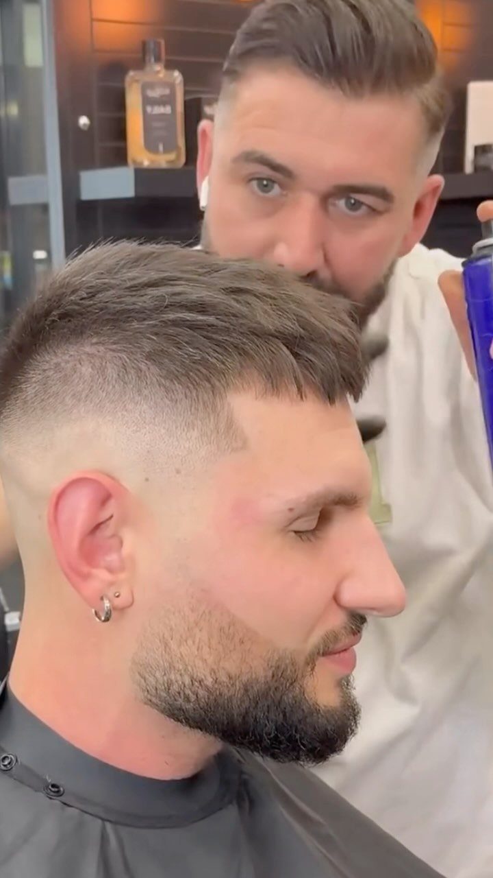 Man with a mid fade haircut and beard getting groomed by a barber.