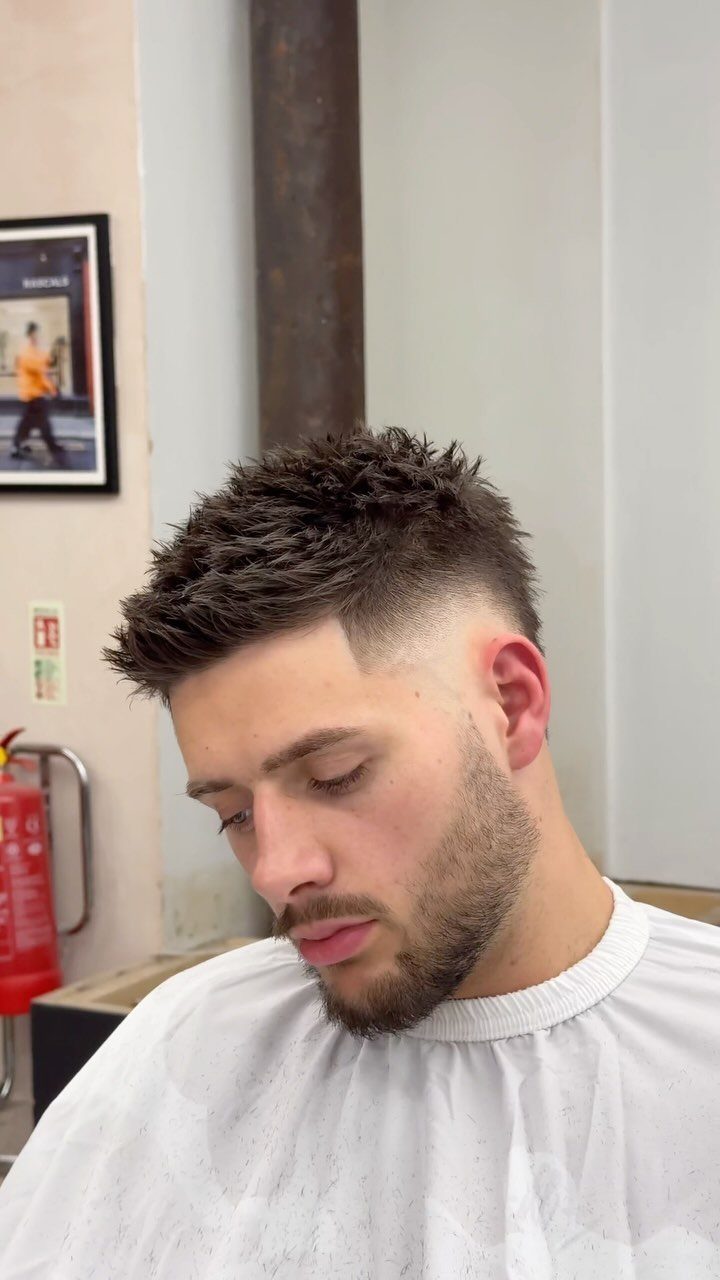 Man with a textured spiky haircut and high skin fade in a barbershop.