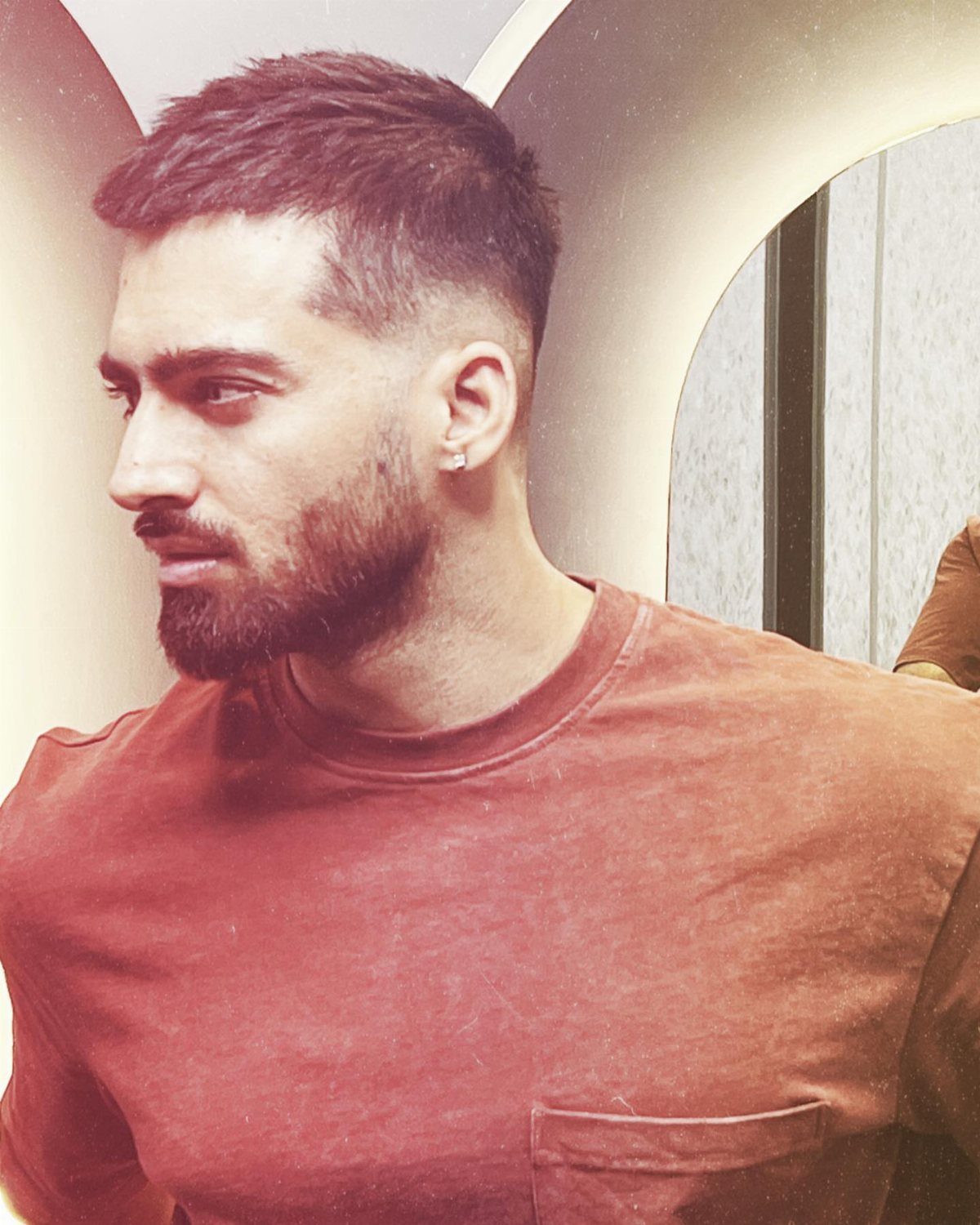 Man with a tightly cropped fade haircut and a groomed beard wearing a brown shirt.