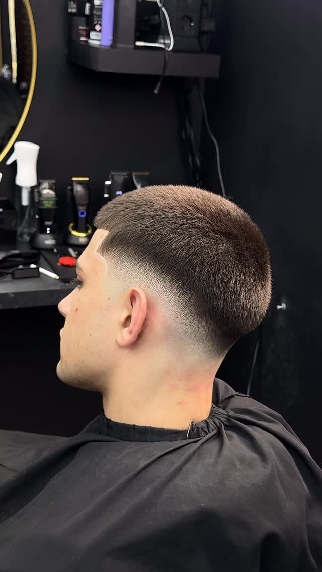 Man with a buzz cut and mid fade haircut wearing a black cape.