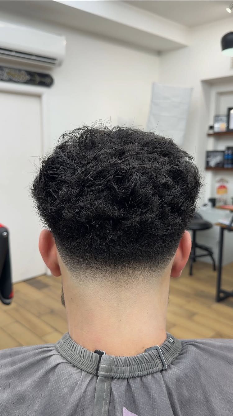 Man with curly hair and a clean taper fade at the nape of his neck.