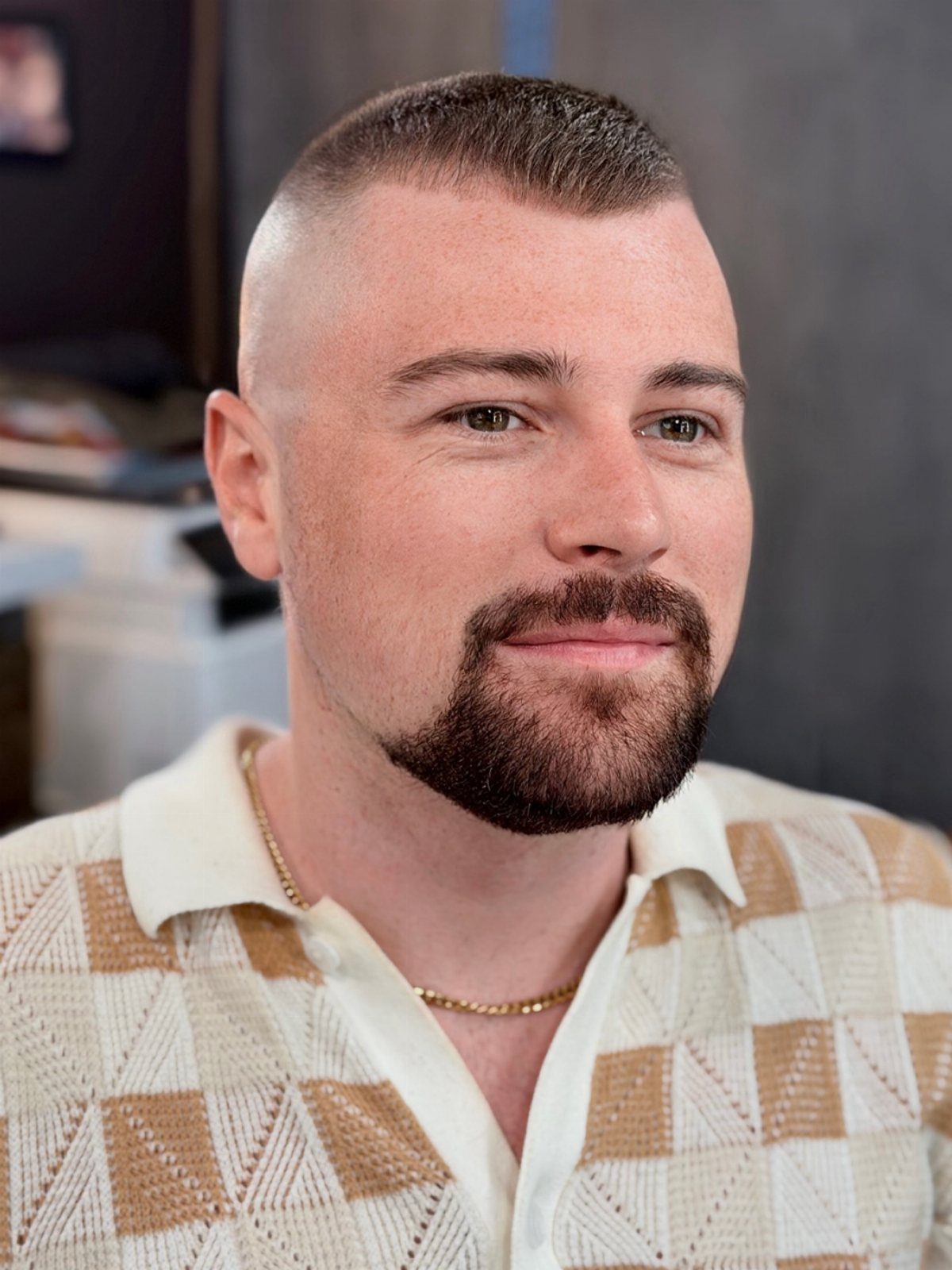 Man with a high fade haircut and groomed goatee wearing a checkered polo shirt.