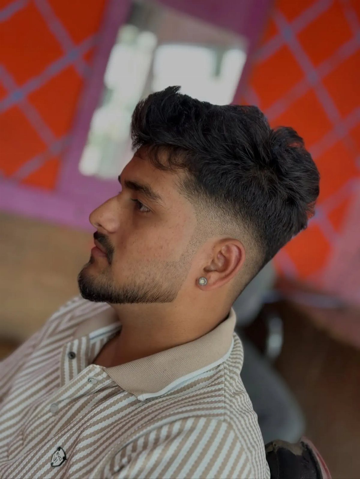 Man with a low fade haircut and groomed beard wearing a striped polo shirt.
