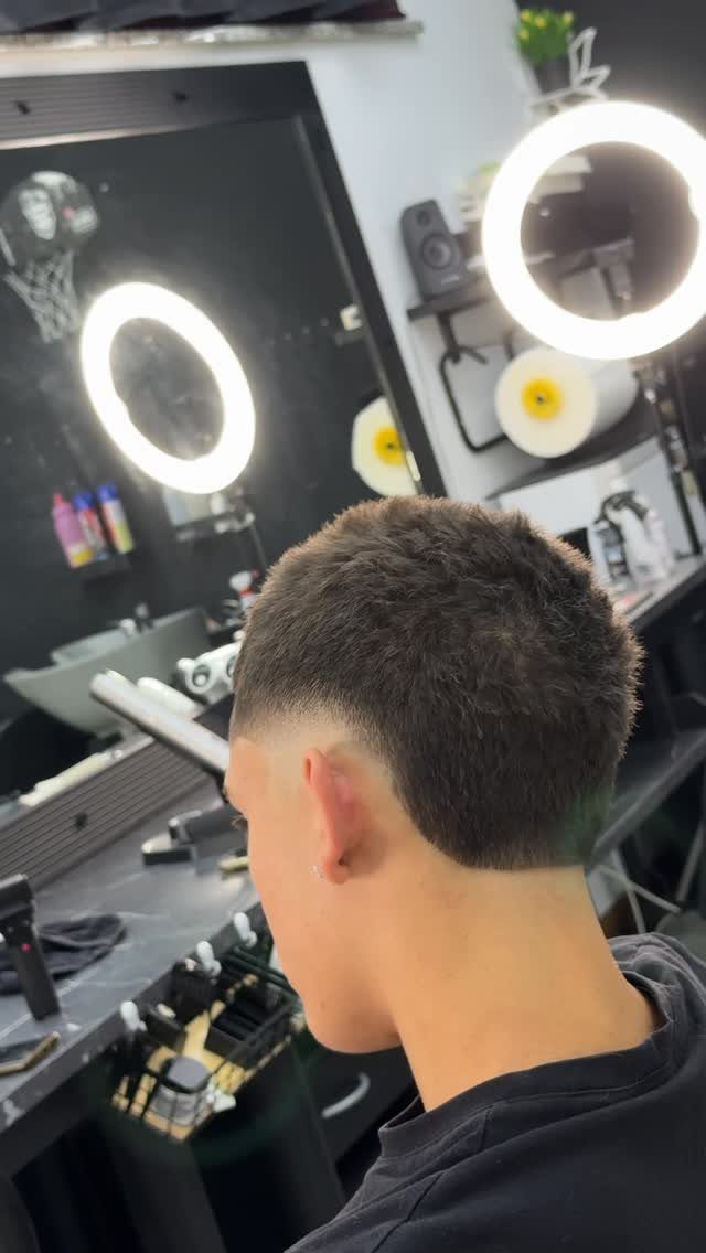 Man with a mid burst fade haircut in a bright barbershop setting.