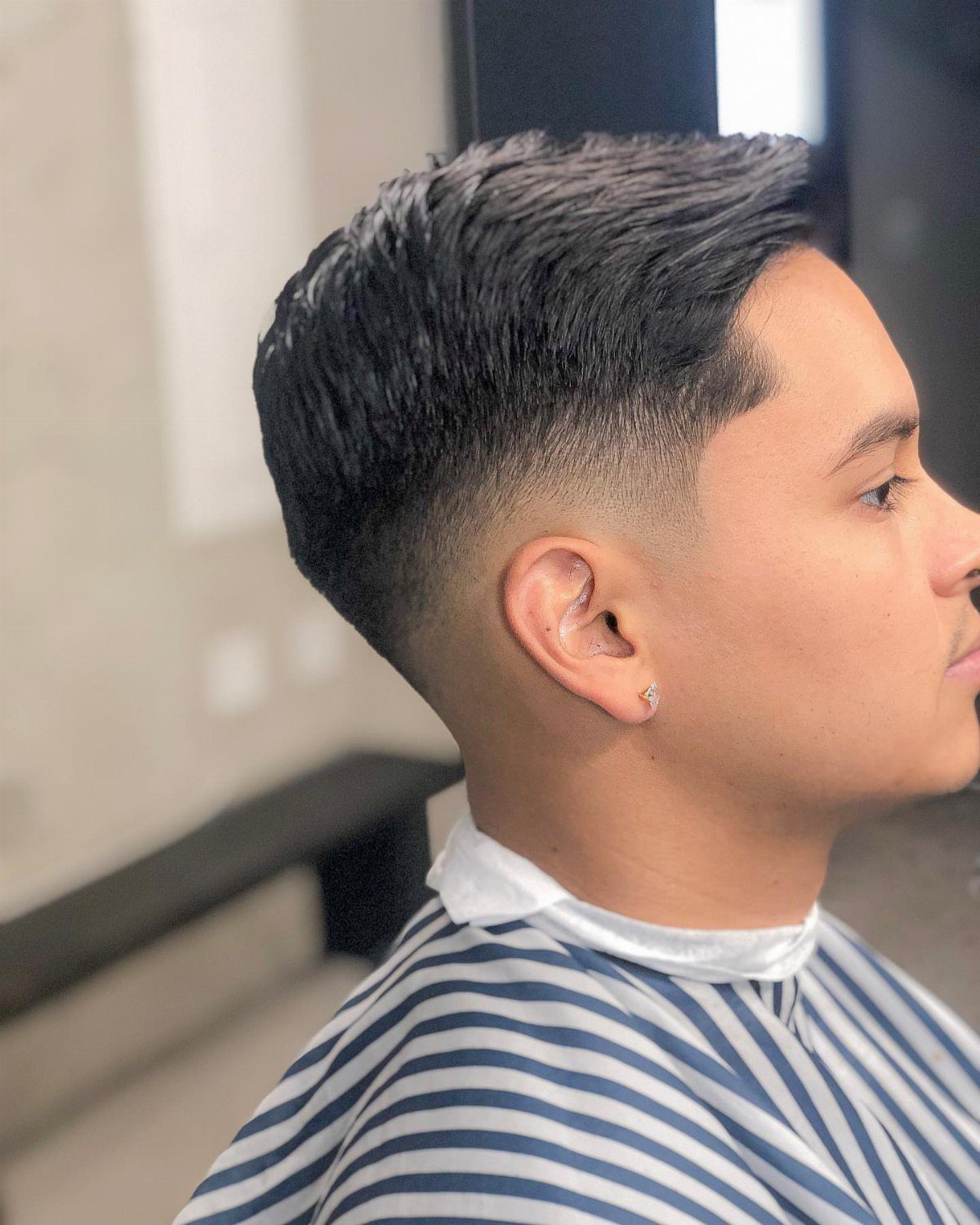 Man with a mid fade comb over hairstyle wearing a striped barber cape.