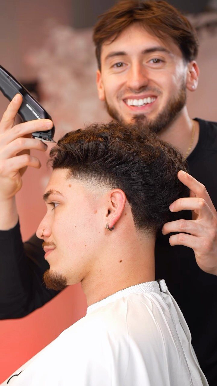 Barber cutting a man's hair into a mid fade taper with textured top.