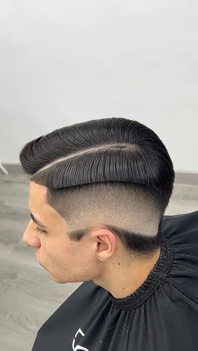 Man with a side part fade haircut and slicked dark hair in a barbershop.