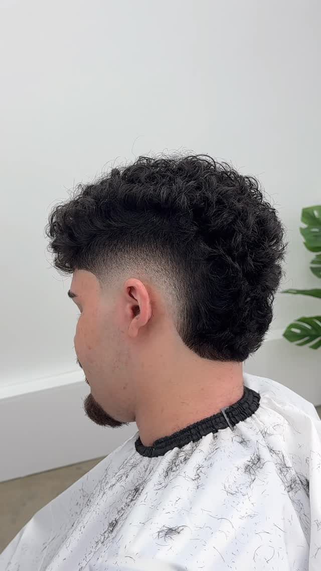 Man with curly black hair featuring a temple fade and a barber cape.