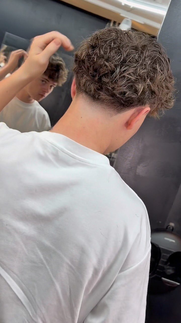 Young man with a textured crop mid fade haircut and wavy brown hair.